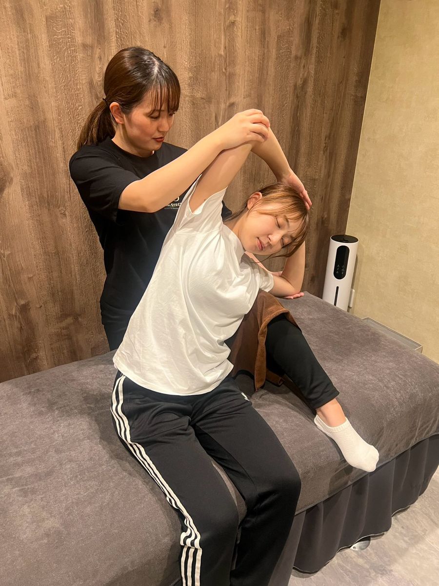 Chill Stretch の完全個室で、トレーナーが女性の腕を支えながら体の側面をゆっくり伸ばしている様子