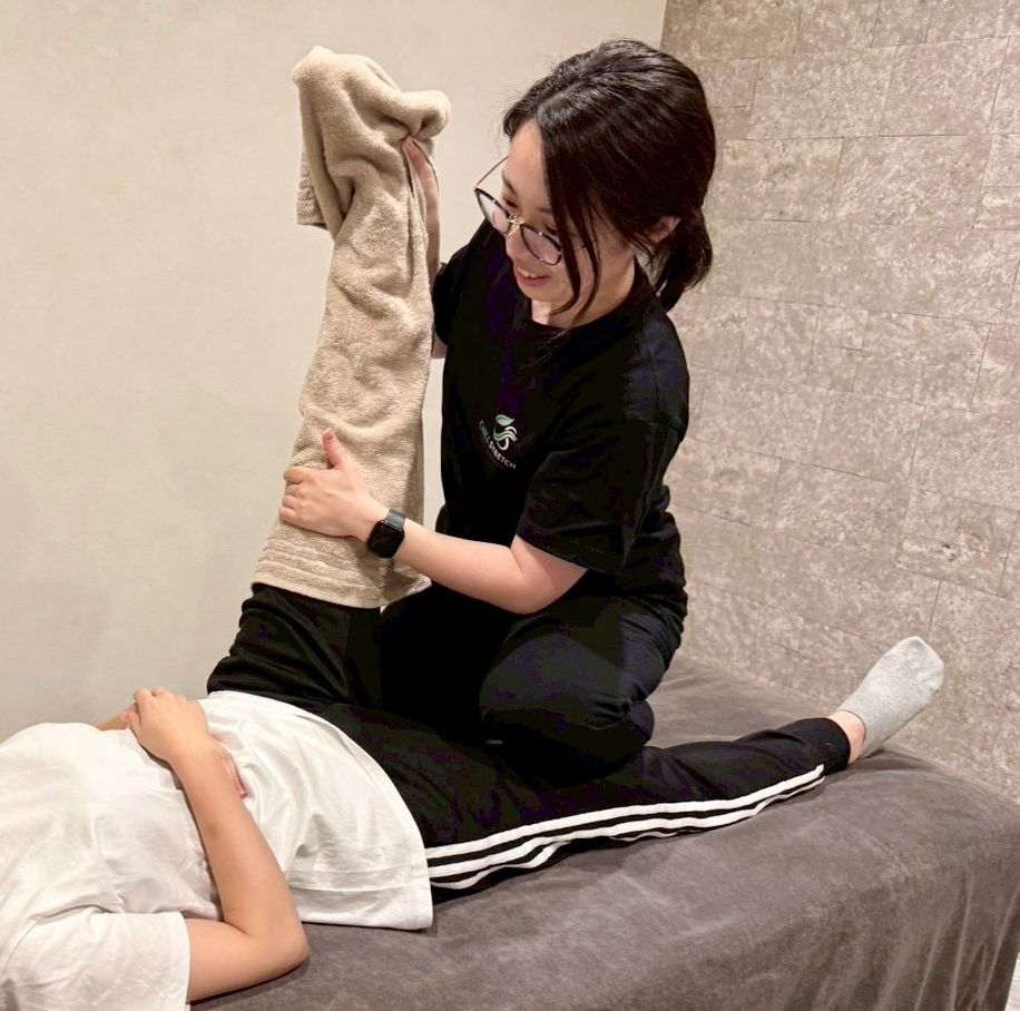 Chill Stretch(浜松市中央区天王町)の完全個室での施術の様子。ベッドの上でトレーナーが脚のストレッチを行っている