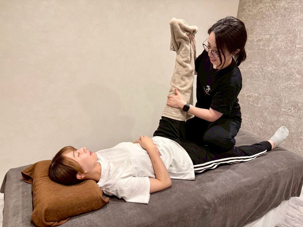 浜松市中央区天王町のストレッチ専門店 Chill Stretch の施術風景。完全個室で仰向けの女性の脚を、トレーナーがタオル越しに支えてゆっくり伸ばしている