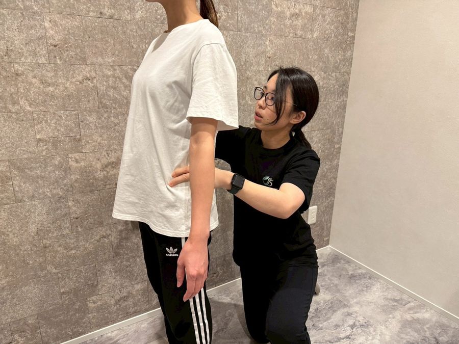 Chill Stretch の姿勢チェック。立った状態でトレーナーが腰と肩の位置を確認している