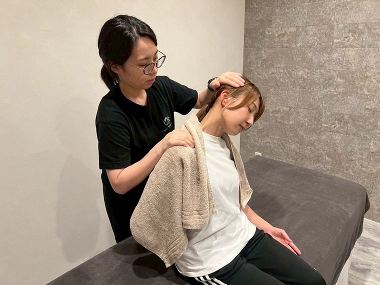 藤森杏菜が、ベッドに座ったお客様の頭を支えて首まわりをゆっくり伸ばしている施術中の様子