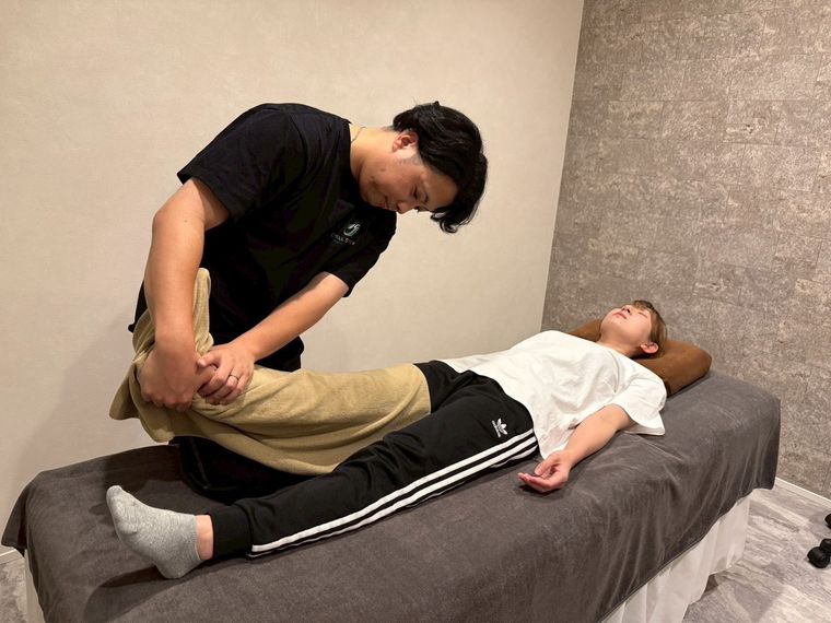 目黒祐樹が、仰向けのお客様の脚を抱えて股関節まわりをゆっくり伸ばしている施術中の様子